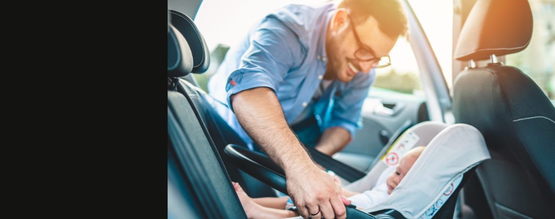 A father smiles while securing infant safely into their car seat