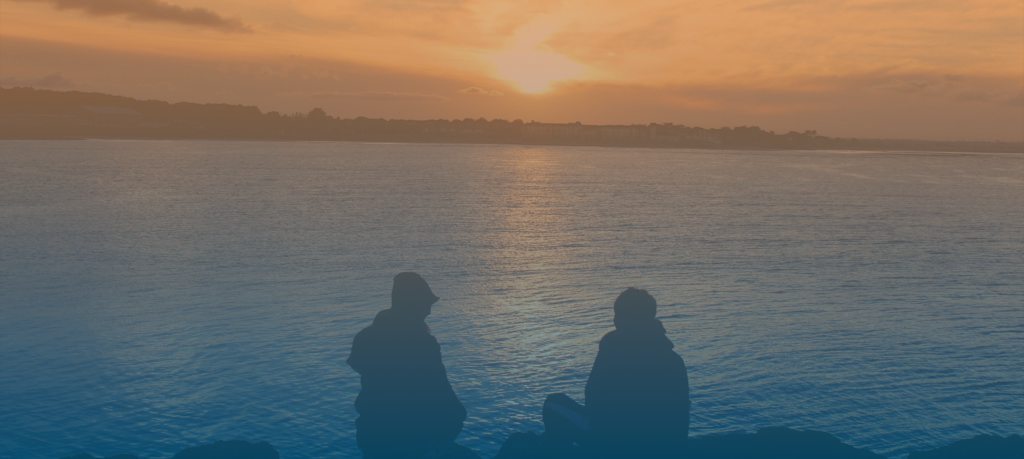 Two individuals sitting in front of a sunset